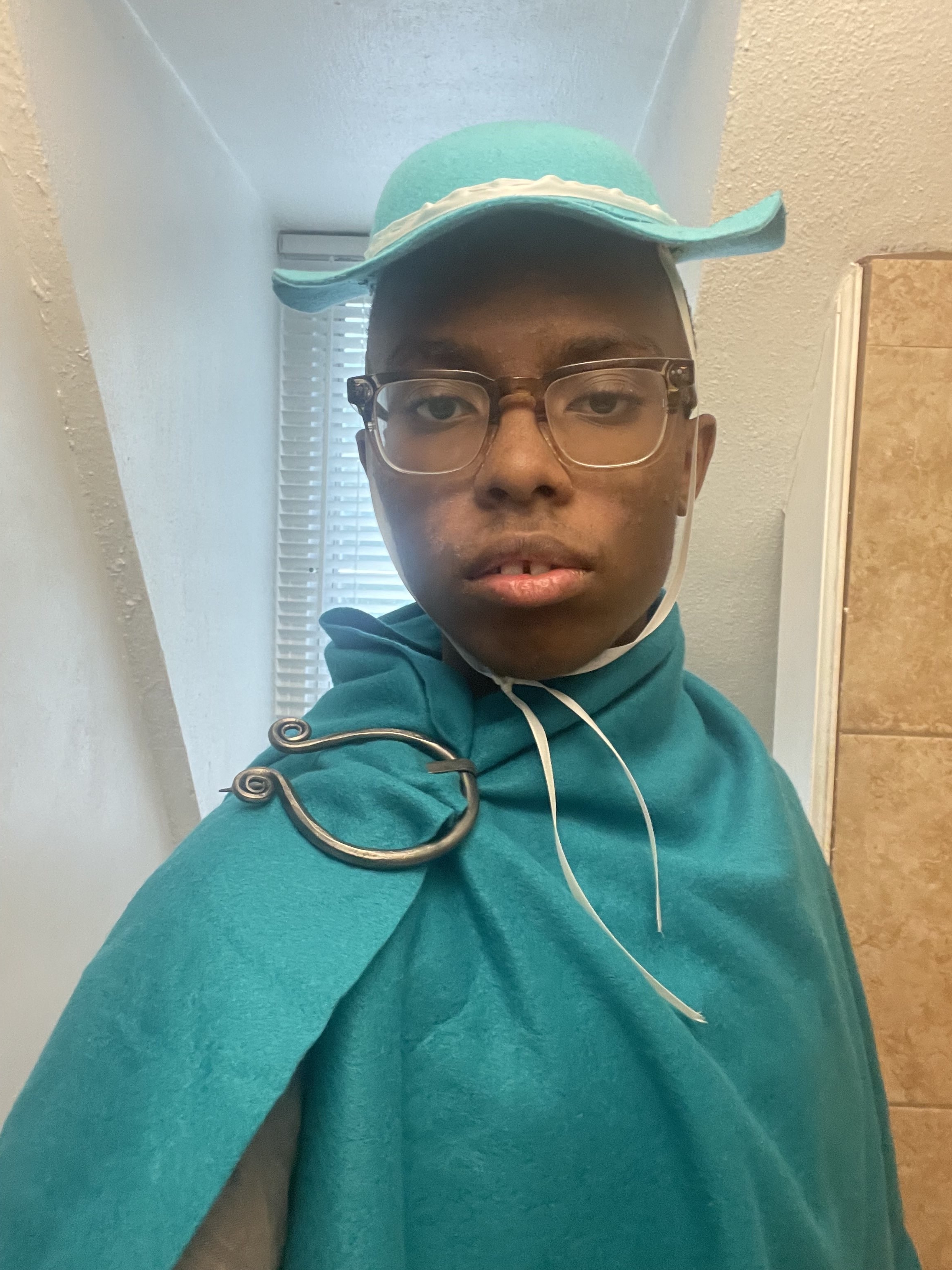 Me, a black man, wearing my petasos, as well as a turquoise cloak with a pewter colored pin